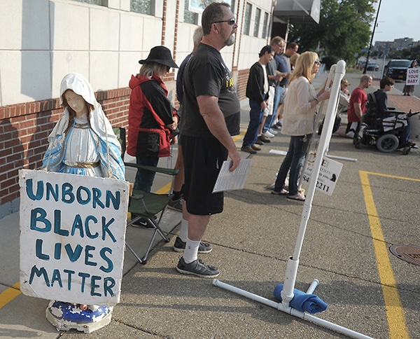 Framed by a statue of Mother Mary, Respect Life Sidewalk advocates protest outside the Woman's Clinic on Main Street. (Dan Cappellazzo/Staff Photographer)